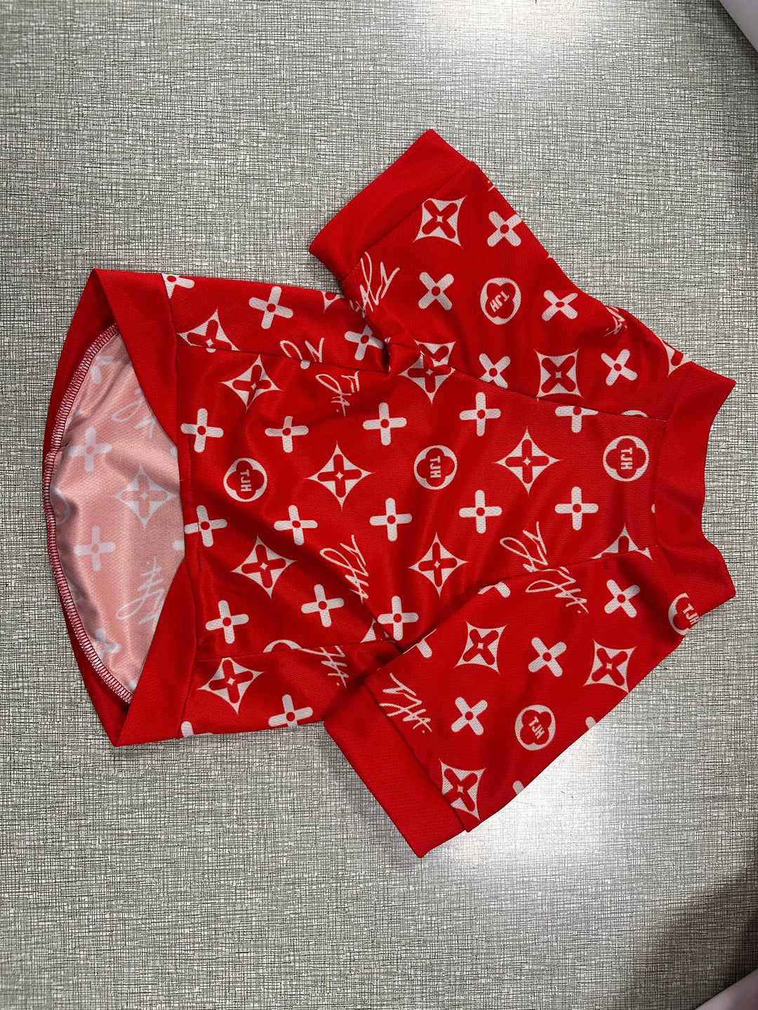 Red pet apparel with a white monogram pattern laid on a grey textured surface