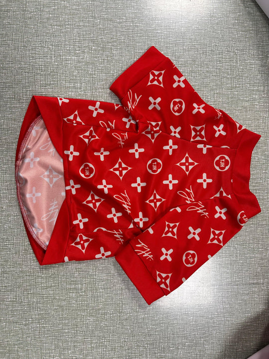 Red pet apparel with a white monogram pattern laid on a grey textured surface