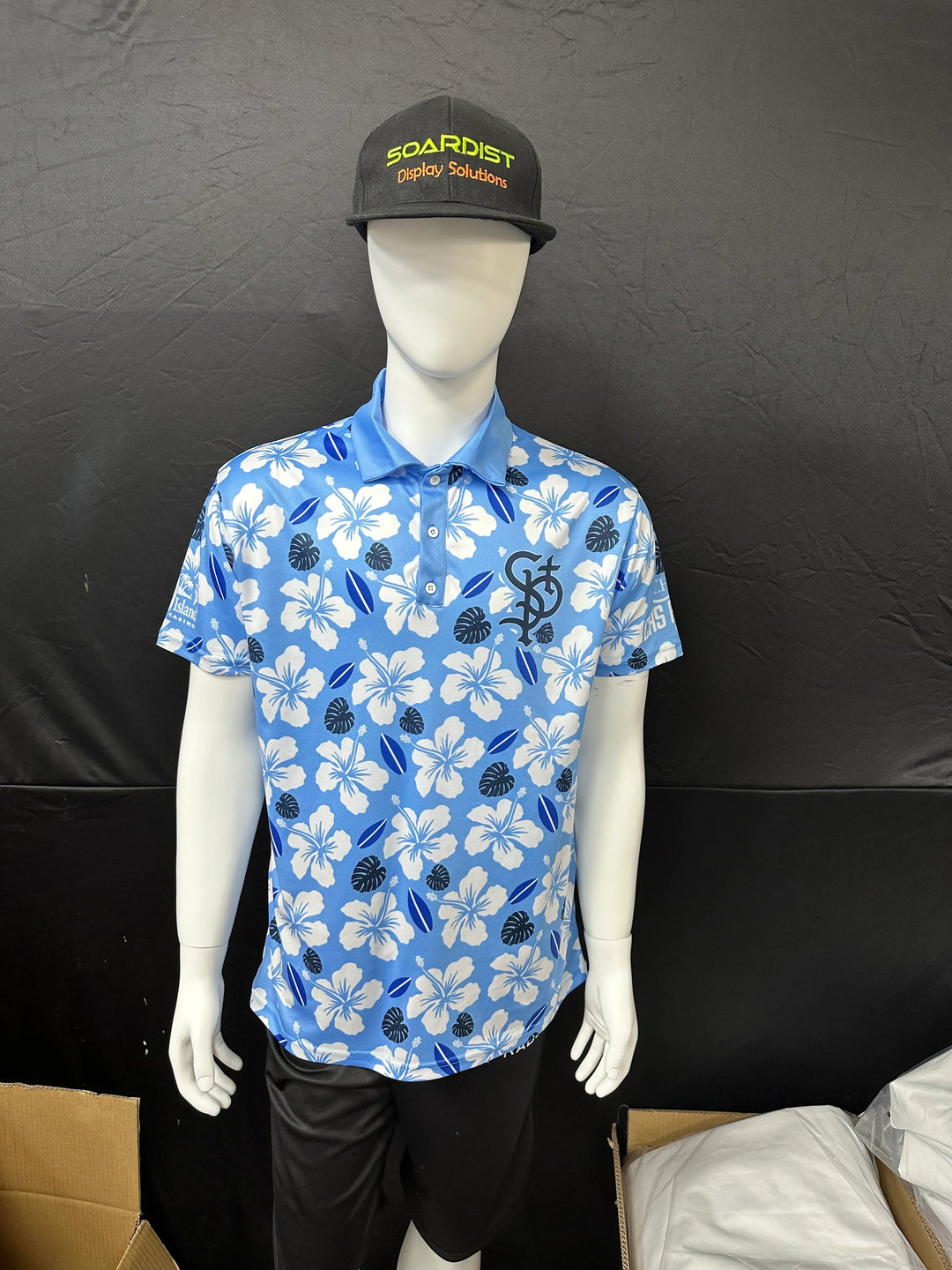 Male mannequin wearing a custom blue floral print polo shirt and a black baseball cap.