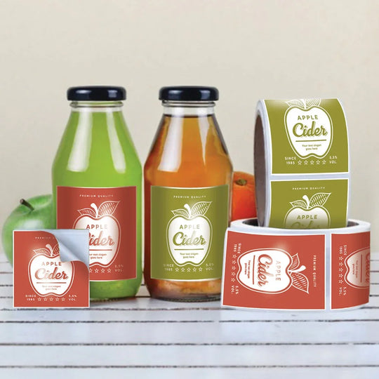 Custom printed apple cider bottle labels and rolls on a white wooden surface.