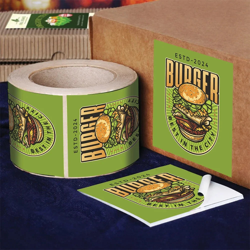 Custom burger logo stickers on a roll, a cardboard box, and a promotional card.