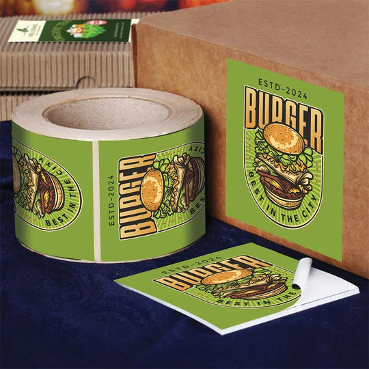 Custom burger logo stickers on a roll, a cardboard box, and a promotional card.