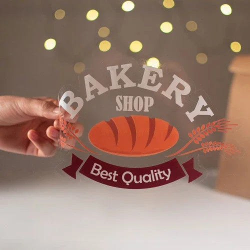 Hand holding a custom transparent bakery shop window decal with a bread illustration.