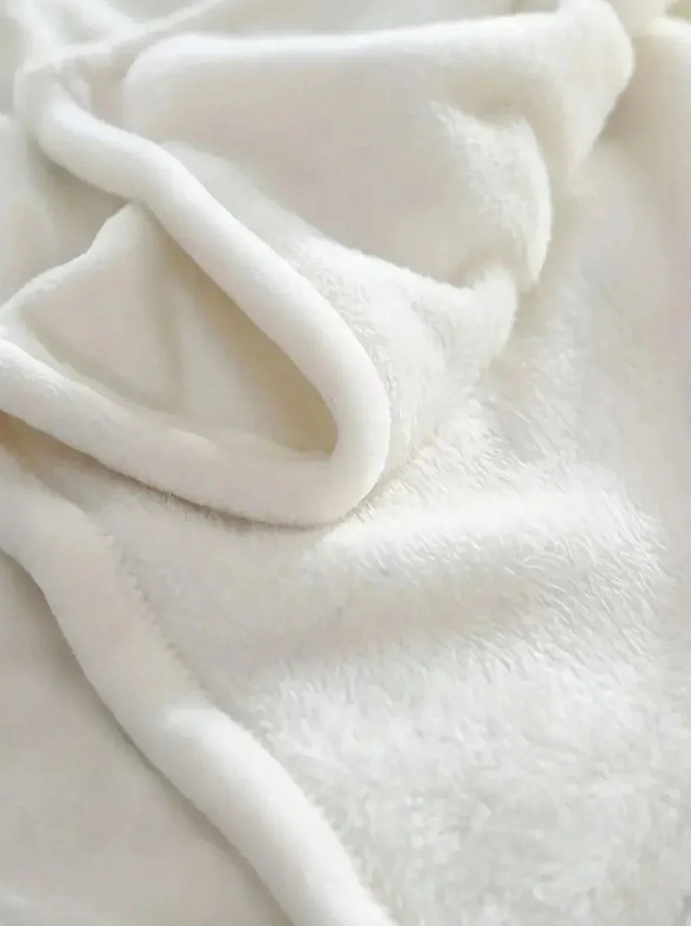 Close-up of a soft, white plush fleece blanket with folded edges.