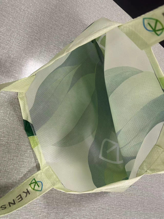 Close-up of a green patterned custom reusable bag with KENS branding on the handle.