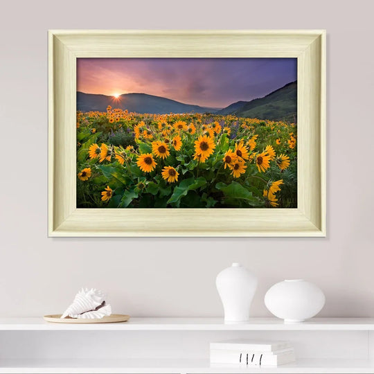 Framed landscape painting of a sunflower field at sunset with mountains in the background.