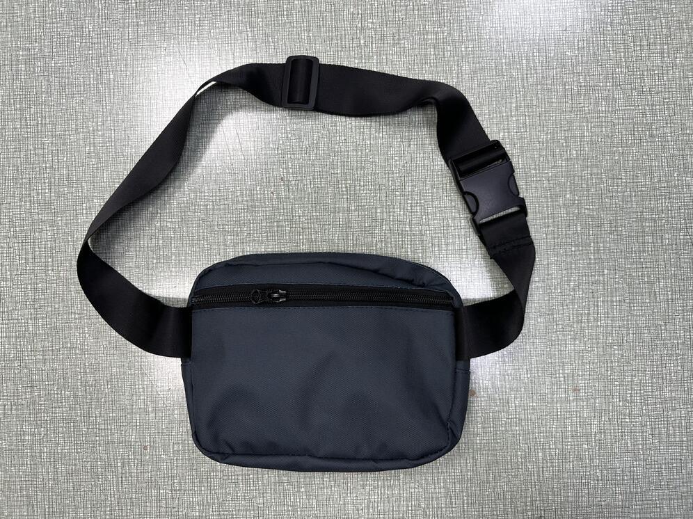 Black nylon waist bag with adjustable strap and zipper pocket on a textured gray surface