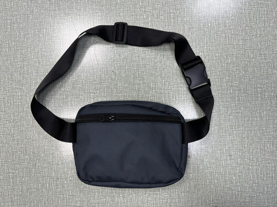 Black nylon waist bag with adjustable strap and zipper pocket on a textured gray surface