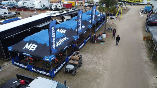 Blue custom MotoBros branded event tents and flags at an outdoor motorsports event