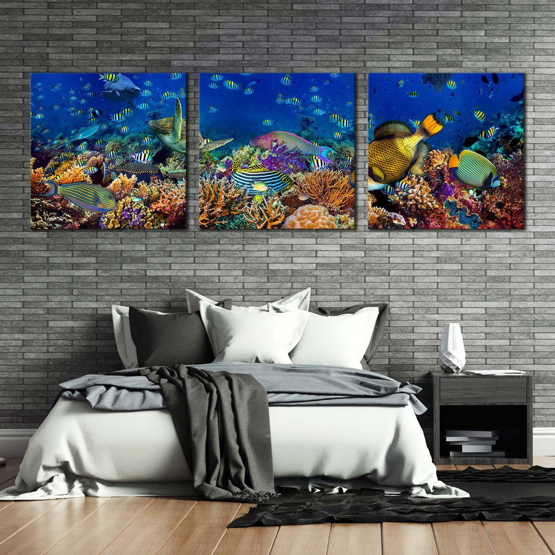 Triptych coral reef fish wall art hanging on a gray brick wall above a modern bed